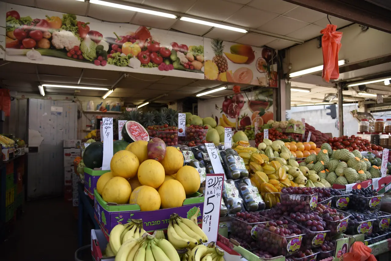 דוכן פירות בשוק הכרמל עם שלטי מחיר בכתב יד. מחוץ למשקפיים התמונה מטושטשת, דרך העדשות היא חדה.